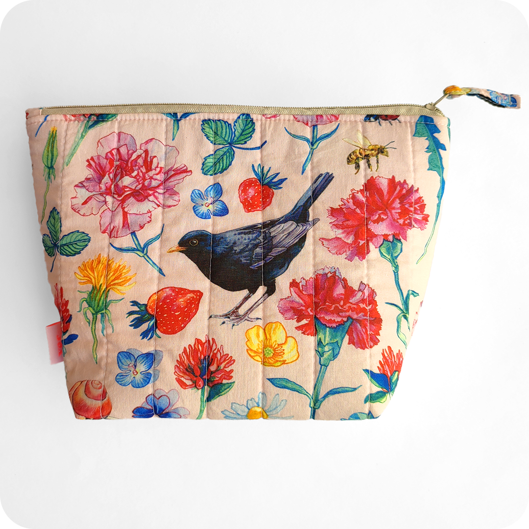 Una trousse realizzata con un tessuto stampato con merli, fiori, foglie, farfalle, coccinelle e api su fondo rosato