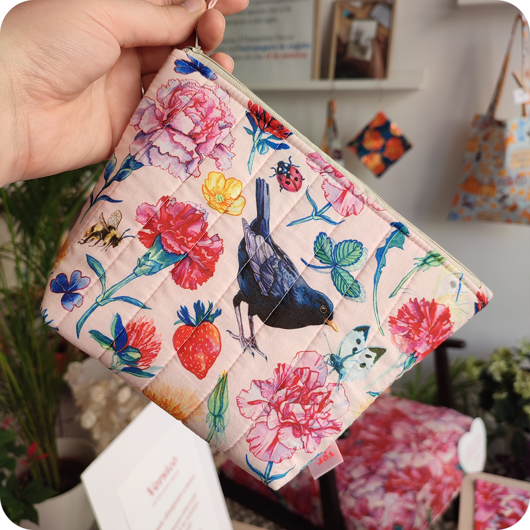 Una trousse realizzata con un tessuto stampato con merli, fiori, foglie, farfalle, coccinelle e api su fondo rosato